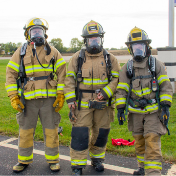 three fire program students wearing fire protective gear and helmets standing outside